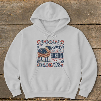 White hoodie with American flag sheep graphic, "Flocks & Freedom Since 1776" text.