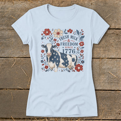 Cow with American flag pattern on shirt surrounded by flowers, text reads "FRESH MILK & FREEDOM SINCE 1776."