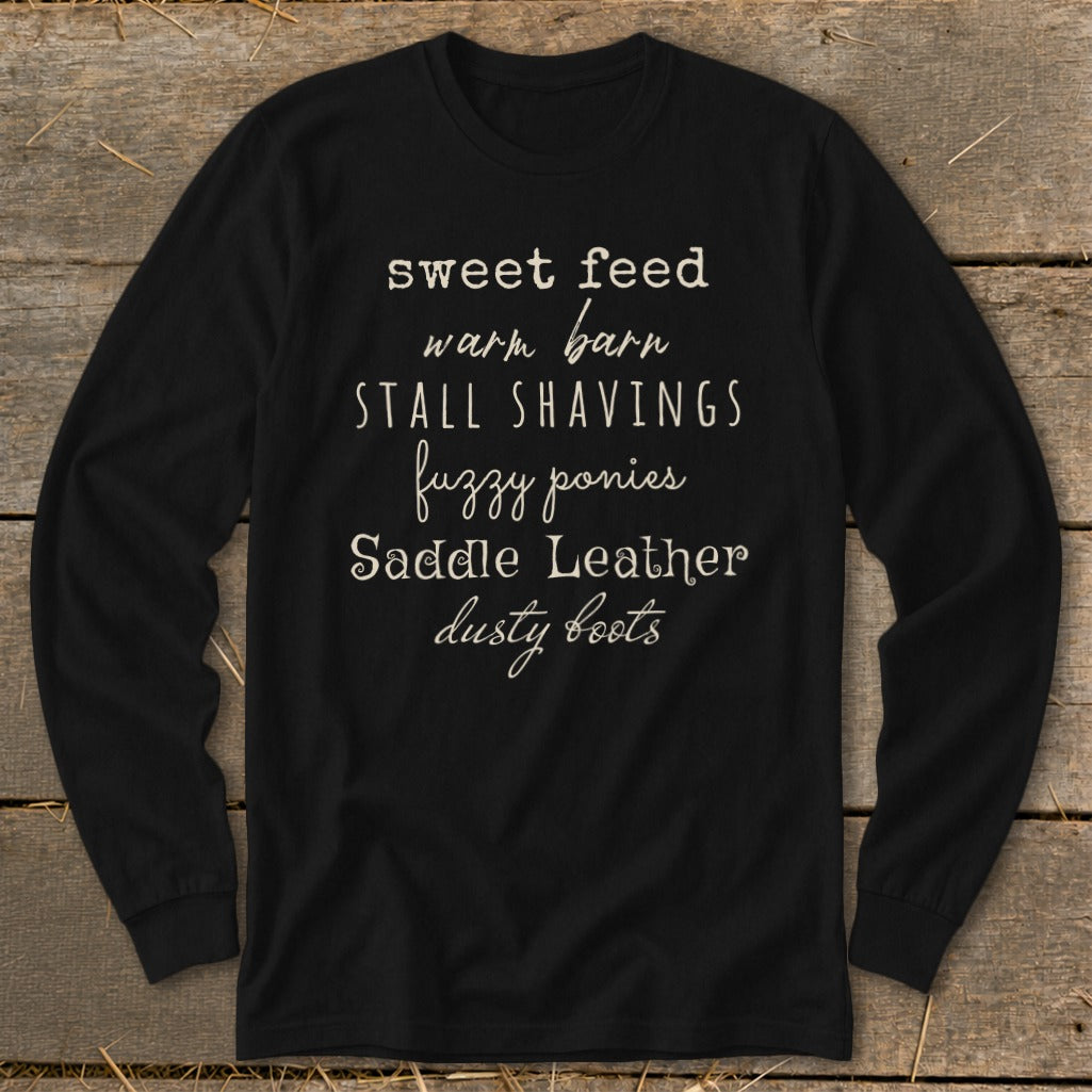 Black long-sleeve shirt with text: sweet feed, warm barn, stall shavings, fuzzy ponies, saddle leather, dusty boots.