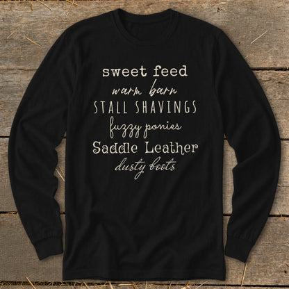 Black long-sleeve shirt with text: sweet feed, warm barn, stall shavings, fuzzy ponies, saddle leather, dusty boots.