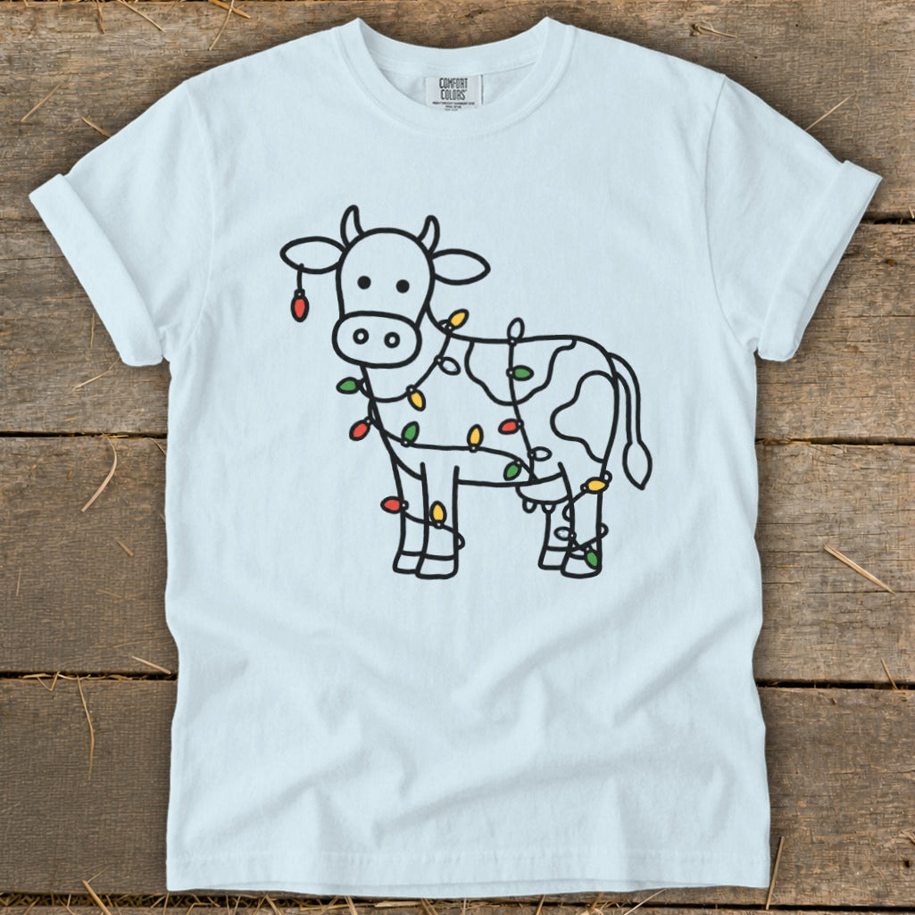 White t-shirt with a cartoon cow wrapped in colorful Christmas lights.