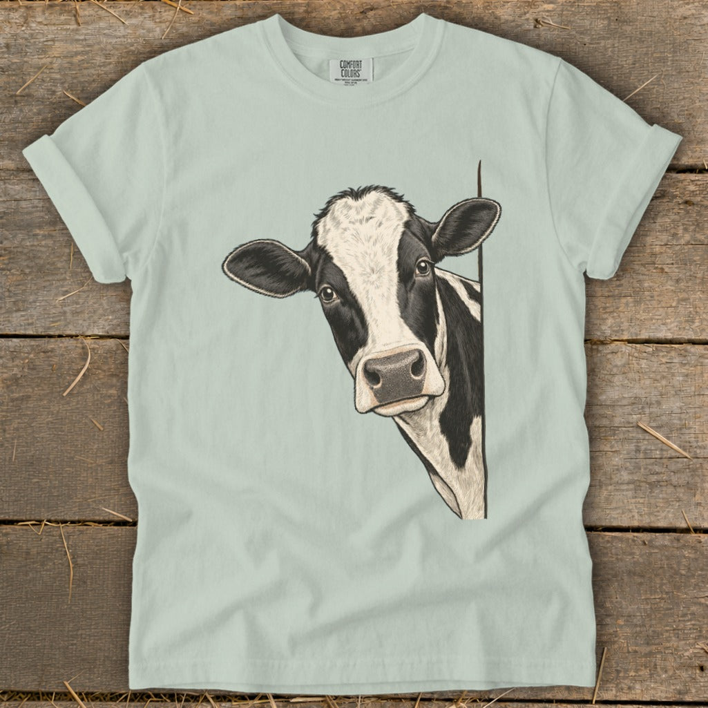 Black and white cow peeking from behind a corner on a light green t-shirt.