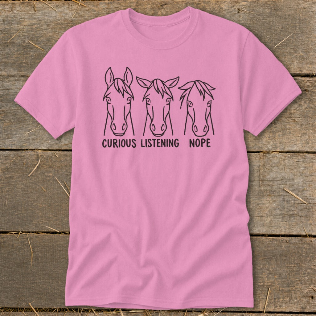 Pink t-shirt with a black line art graphic of three horse heads and the text "CURIOUS LISTENING NOPE."