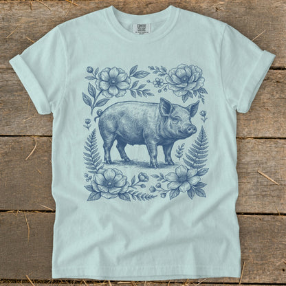 Light blue t-shirt with a blue line drawing of a pig surrounded by flowers and ferns.