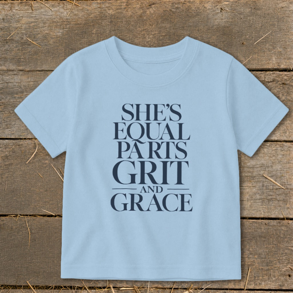 Light blue t-shirt with navy text "SHE'S EQUAL PARTS GRIT AND GRACE".