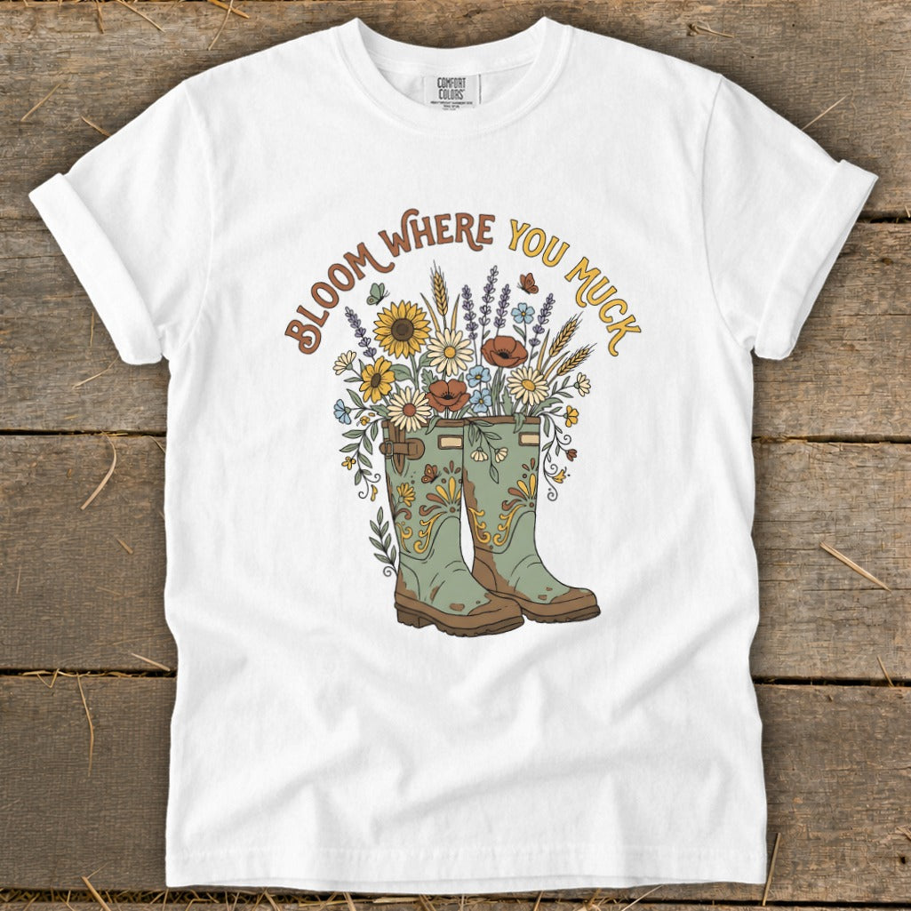 White t-shirt with "Bloom Where You Muck" text over gardening boots and flowers.