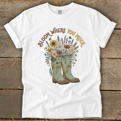 White t-shirt with "Bloom Where You Muck" text over gardening boots and flowers.