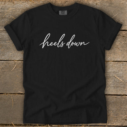 Black Comfort Colors t-shirt with white "heels down" script graphic.