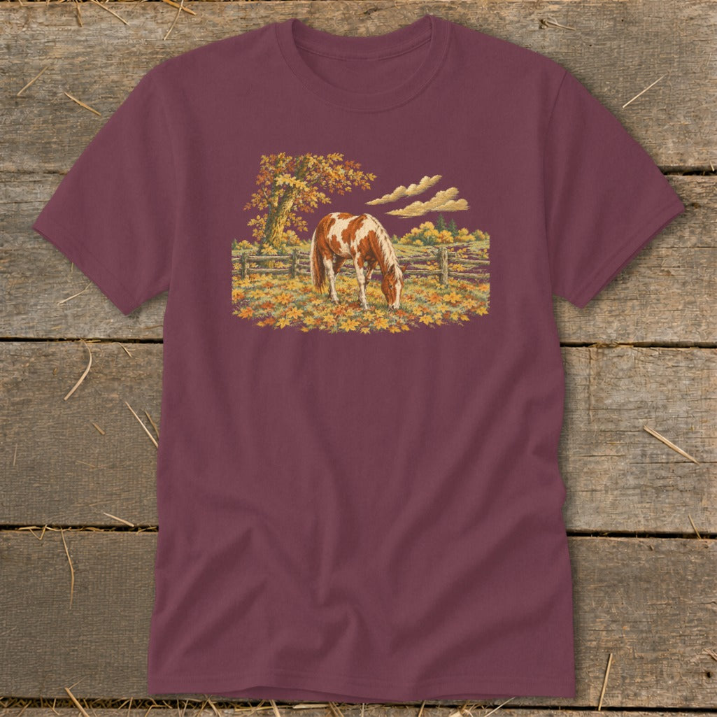 Brown and white horse grazing in a field of autumn leaves by a wooden fence.