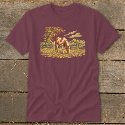 Brown and white horse grazing in a field of autumn leaves by a wooden fence.