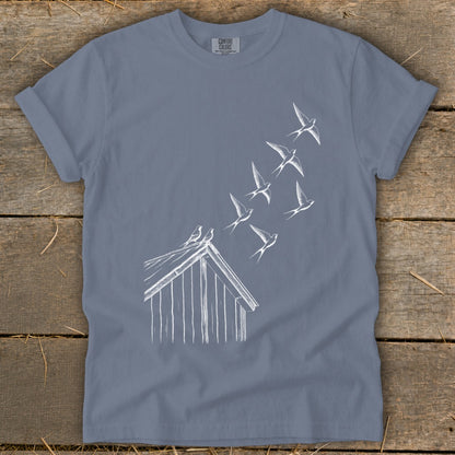 A slate blue crewneck t-shirt featuring a white line drawing of birds flying from a birdhouse roof.