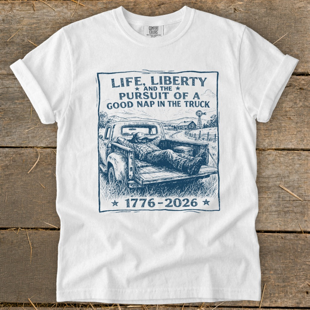 White t-shirt with graphic of man napping in truck bed, reads "Life, Liberty, Pursuit of a Good Nap".