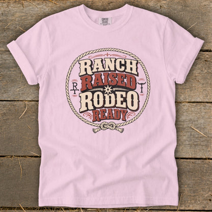 A light pink t-shirt featuring a circular western graphic that reads Ranch Raised Rodeo Ready.