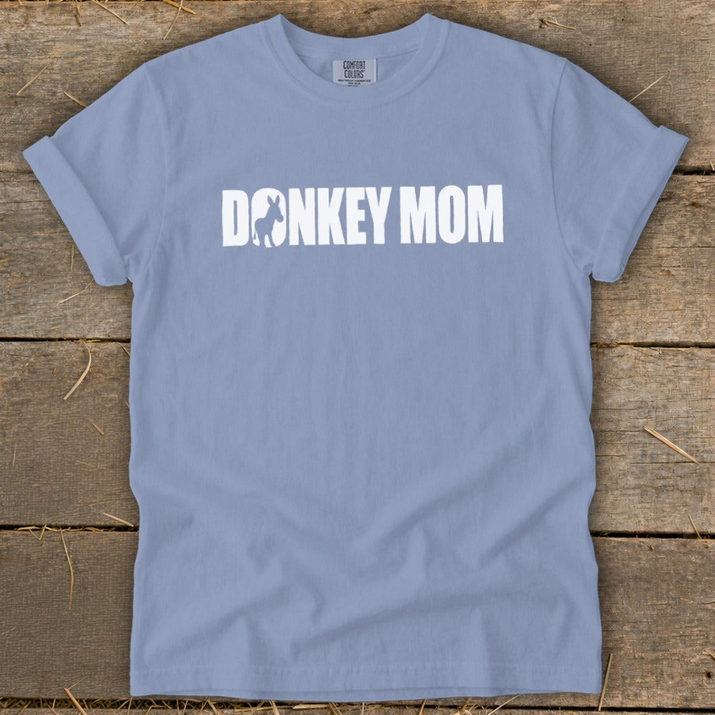 A periwinkle blue short-sleeve t-shirt with white text reading "DONKEY MOM" laid flat on a wooden surface.