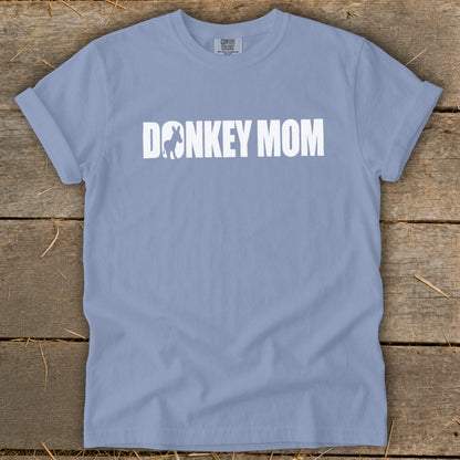 A periwinkle blue short-sleeve t-shirt with white text reading "DONKEY MOM" laid flat on a wooden surface.