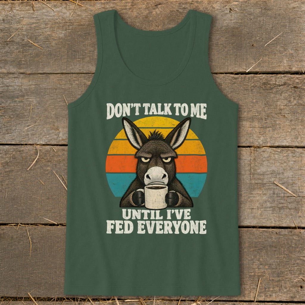 A green tank top featuring a graphic of a grumpy donkey holding a coffee mug and text that reads don't talk to me until i've fed everyone.