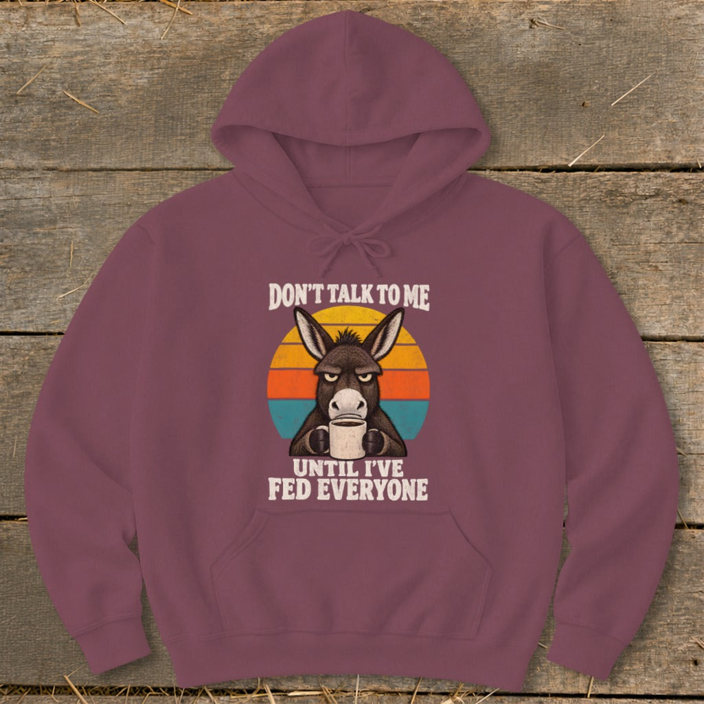 A maroon hoodie featuring a grumpy donkey drinking coffee against a retro sunset graphic with text.