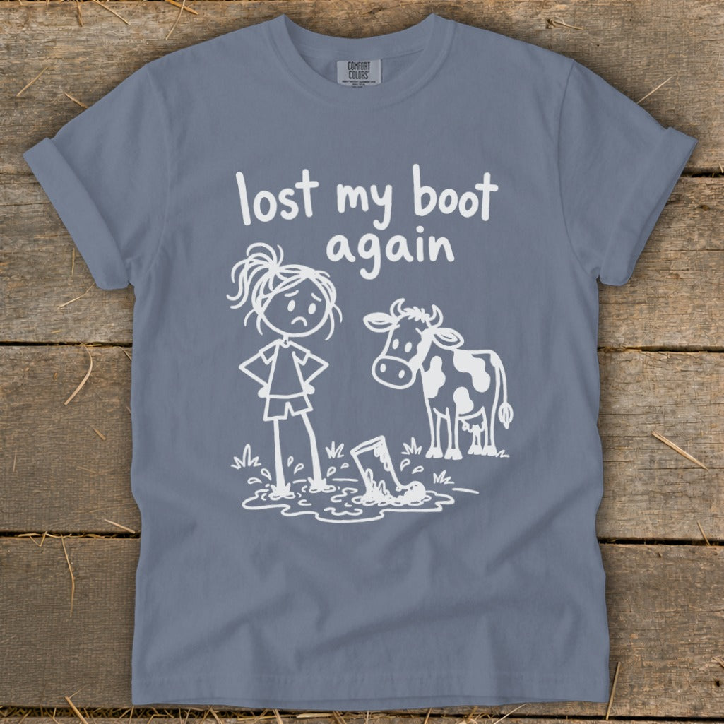 A blue-gray crewneck t-shirt with a white graphic of a sad stick-figure girl and cow looking at a muddy boot, with text reading "lost my boot again".