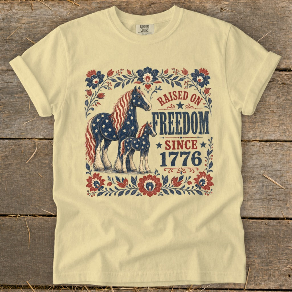Light yellow t-shirt with horses and "Raised on Freedom Since 1776" text.