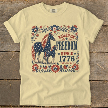Light yellow t-shirt with horses and "Raised on Freedom Since 1776" text.