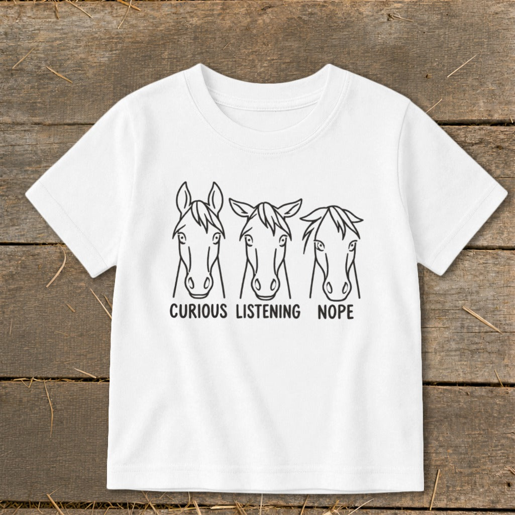 A white t-shirt featuring a black graphic of three horse heads with the text "CURIOUS," "LISTENING," and "NOPE."