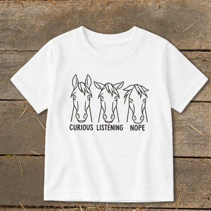 A white t-shirt featuring a black graphic of three horse heads with the text "CURIOUS," "LISTENING," and "NOPE."