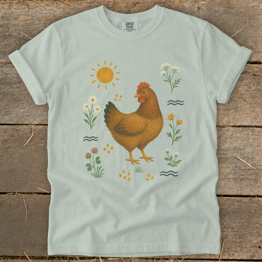 Light blue t-shirt with illustration of a brown hen surrounded by sun, flowers, and wavy lines.