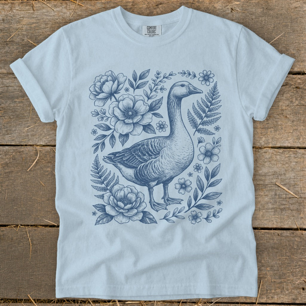 Light blue t-shirt with a blue ink drawing of a goose surrounded by flowers and foliage.