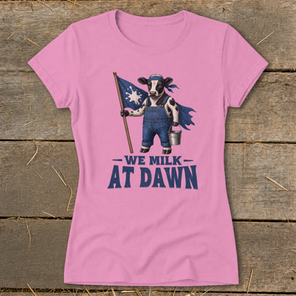 Pink t-shirt with cow in overalls holding flag and bucket, text "WE MILK AT DAWN".