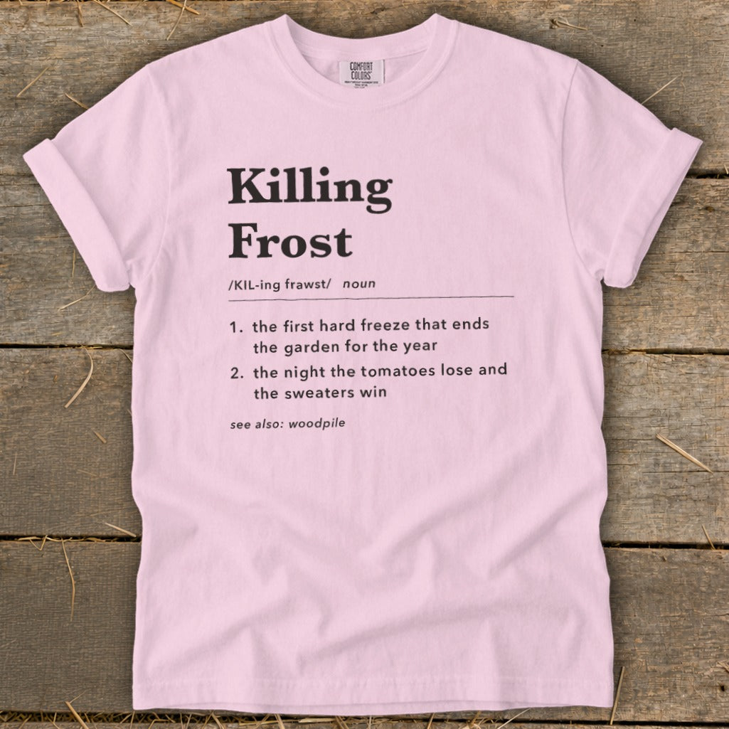 Light pink t-shirt featuring dictionary-style text defining the term Killing Frost, laid flat on a wooden surface.
