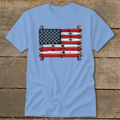 A light blue crewneck t-shirt featuring a rustic American flag design made of weathered wood planks and horseshoes.