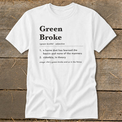 White t-shirt printed with a humorous dictionary-style definition of Green Broke, displayed on a rustic wooden background.