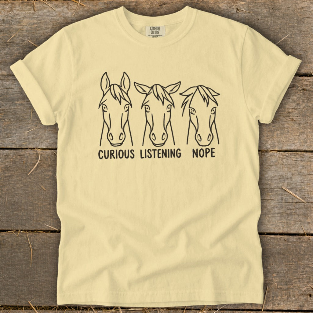 A light yellow t-shirt features three line-drawing horse heads with the text "CURIOUS," "LISTENING," and "NOPE."
