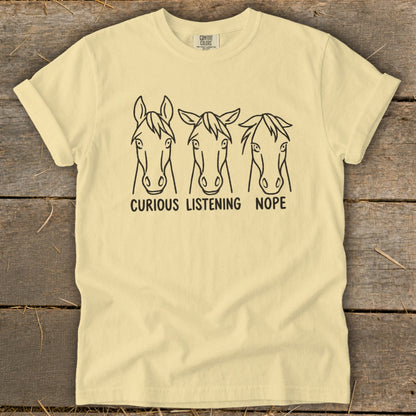 A light yellow t-shirt features three line-drawing horse heads with the text "CURIOUS," "LISTENING," and "NOPE."