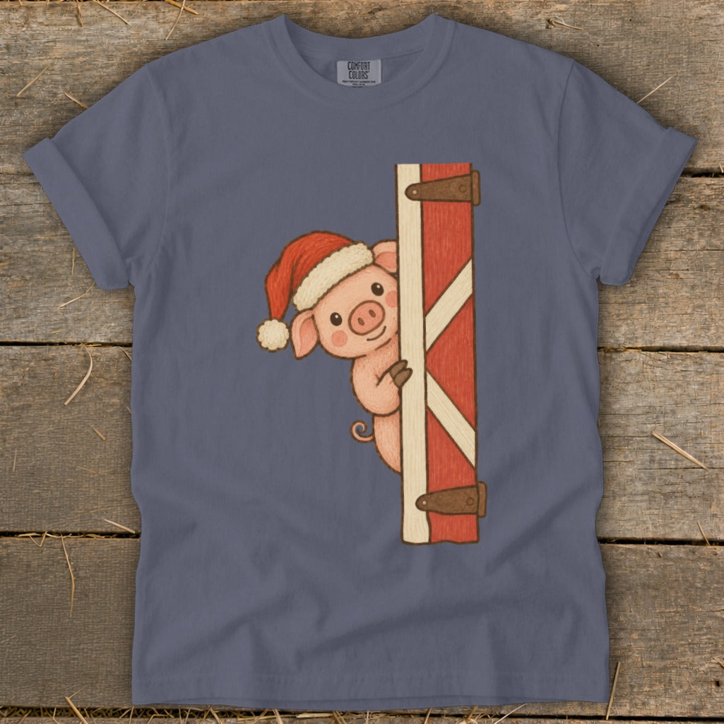 Pig wearing Santa hat peeking around barn door graphic on blue t-shirt.