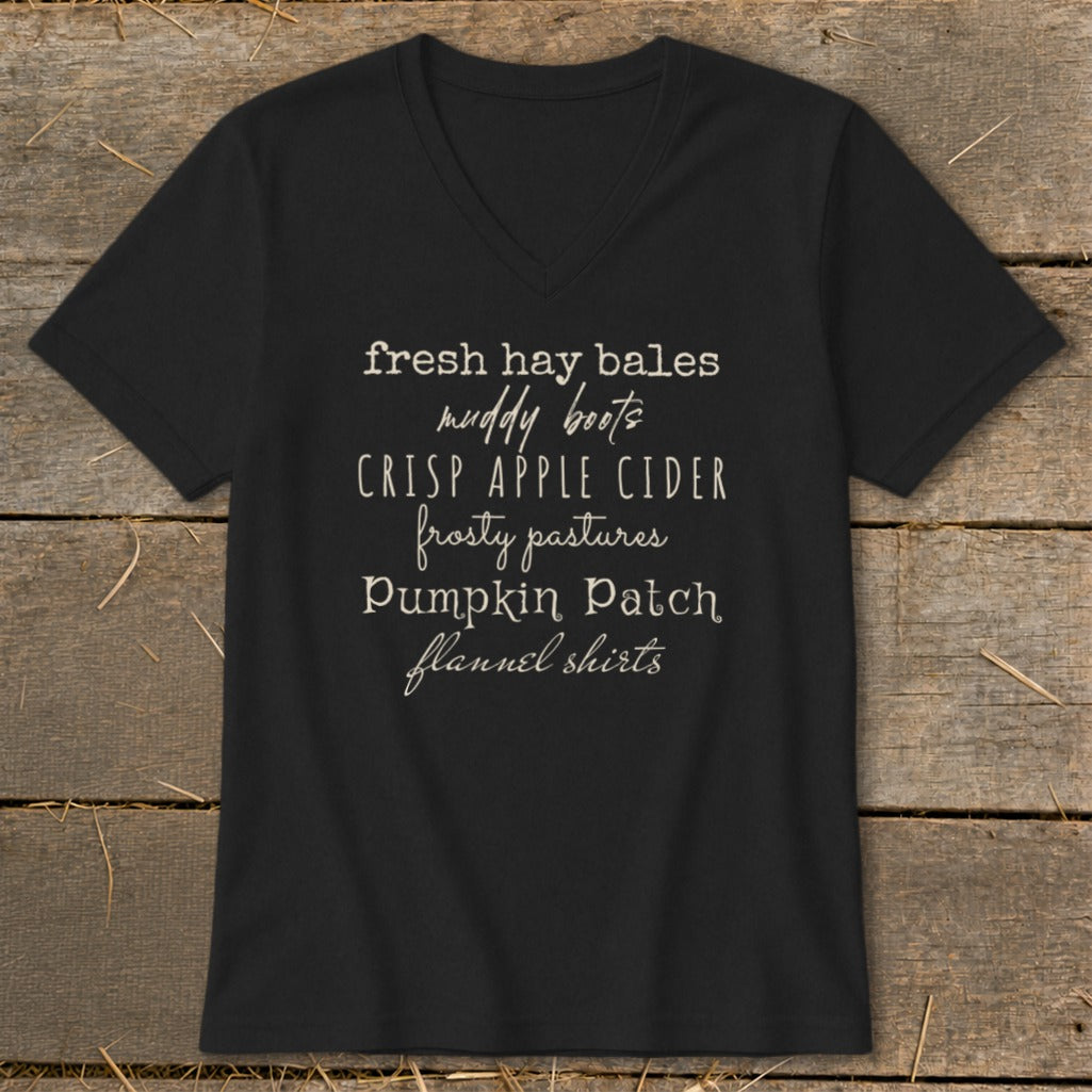 Black v-neck shirt with fall-themed text listing: fresh hay bales, muddy boots, crisp apple cider.