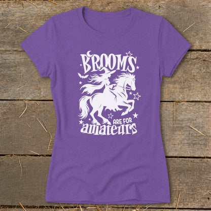 Purple t-shirt with white graphic of witch on horse, text "Brooms are for amateurs".
