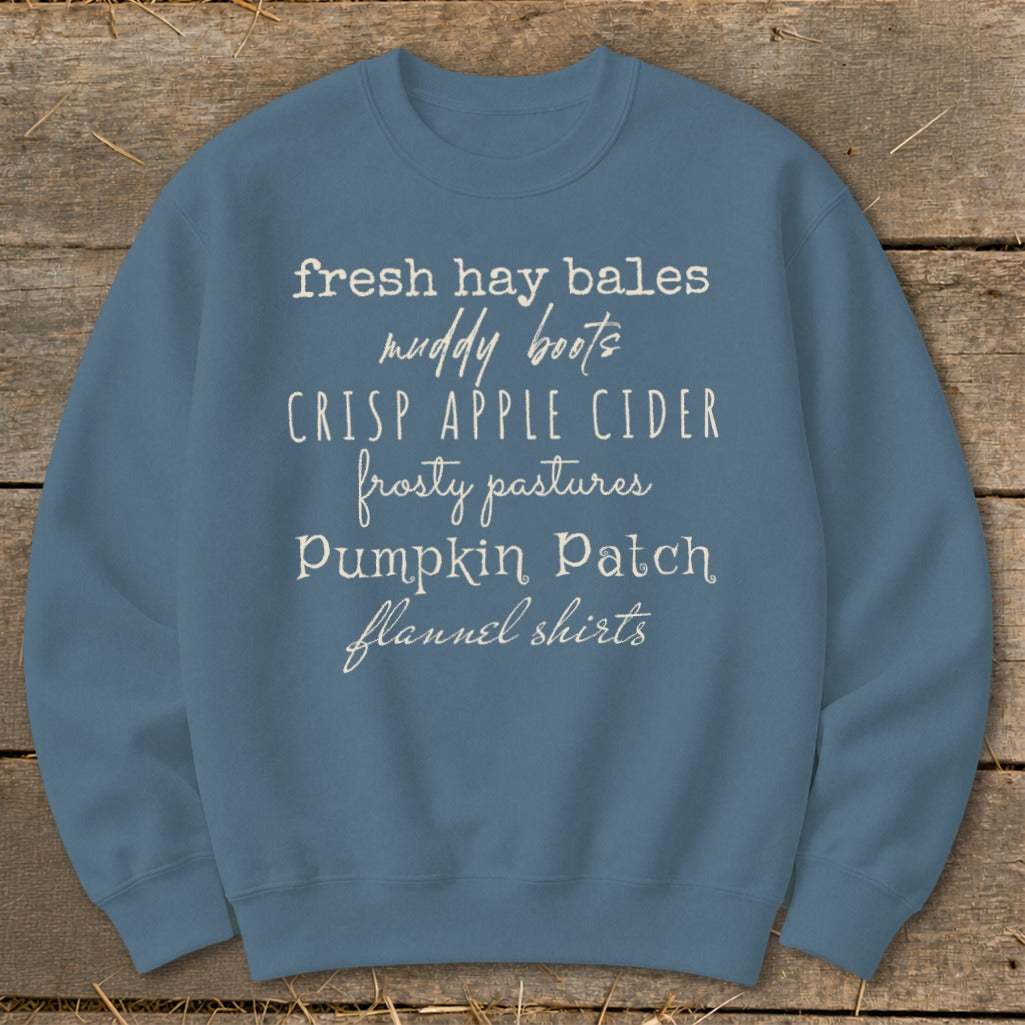 Blue sweatshirt with white text listing "fresh hay bales, muddy boots, crisp apple cider, frosty pastures, pumpkin patch, flannel shirts."