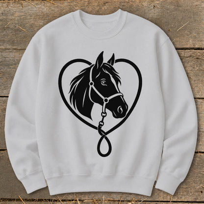 Light gray crewneck sweatshirt centered on a wooden surface, featuring a black graphic of a horse's head framed by a heart shape.