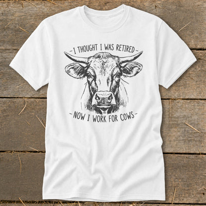 White t-shirt with a sketch of a cow and text "I THOUGHT I WAS RETIRED - NOW I WORK FOR COWS".