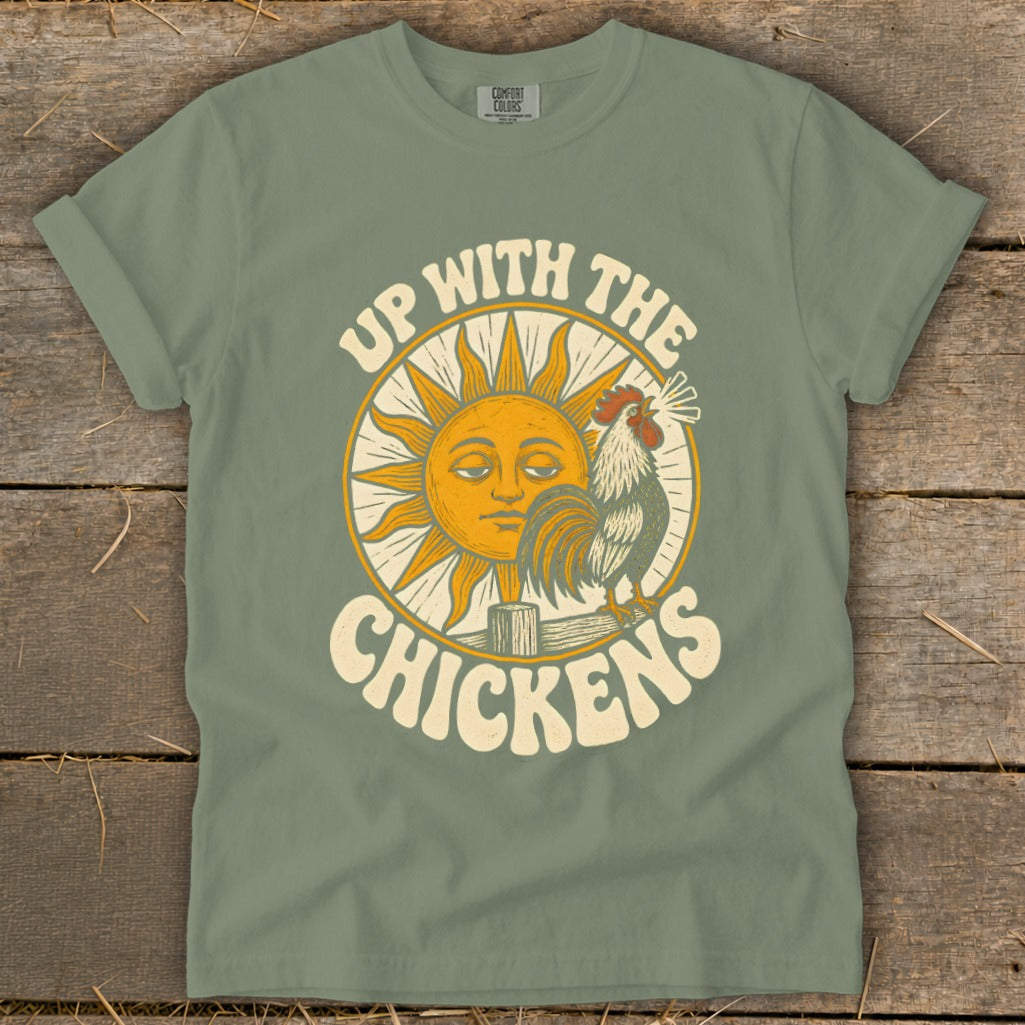 An olive green t-shirt with a vintage graphic of a rooster, a smiling sun, and the text Up With The Chickens.