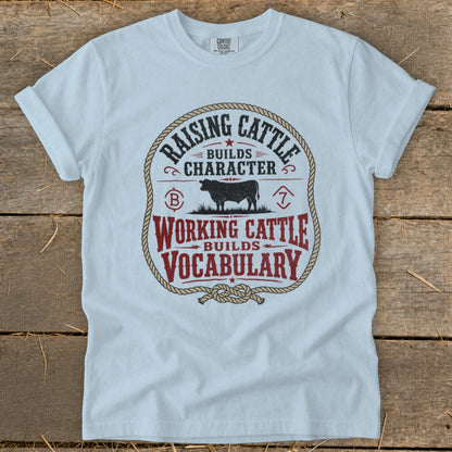 Light blue t-shirt with "Raising Cattle Builds Character, Working Cattle Builds Vocabulary" text and cow graphic.