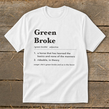 A white t-shirt featuring dictionary-style text defining the term green broke laid flat on a wooden background.