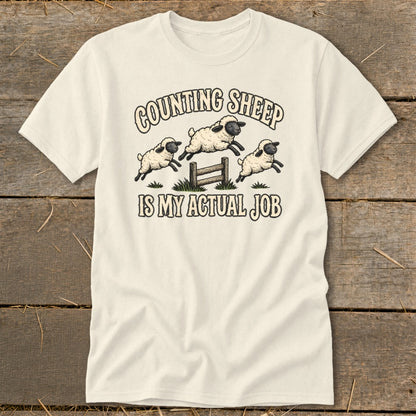 Cream t-shirt with sheep jumping fence and text "Counting Sheep Is My Actual Job."