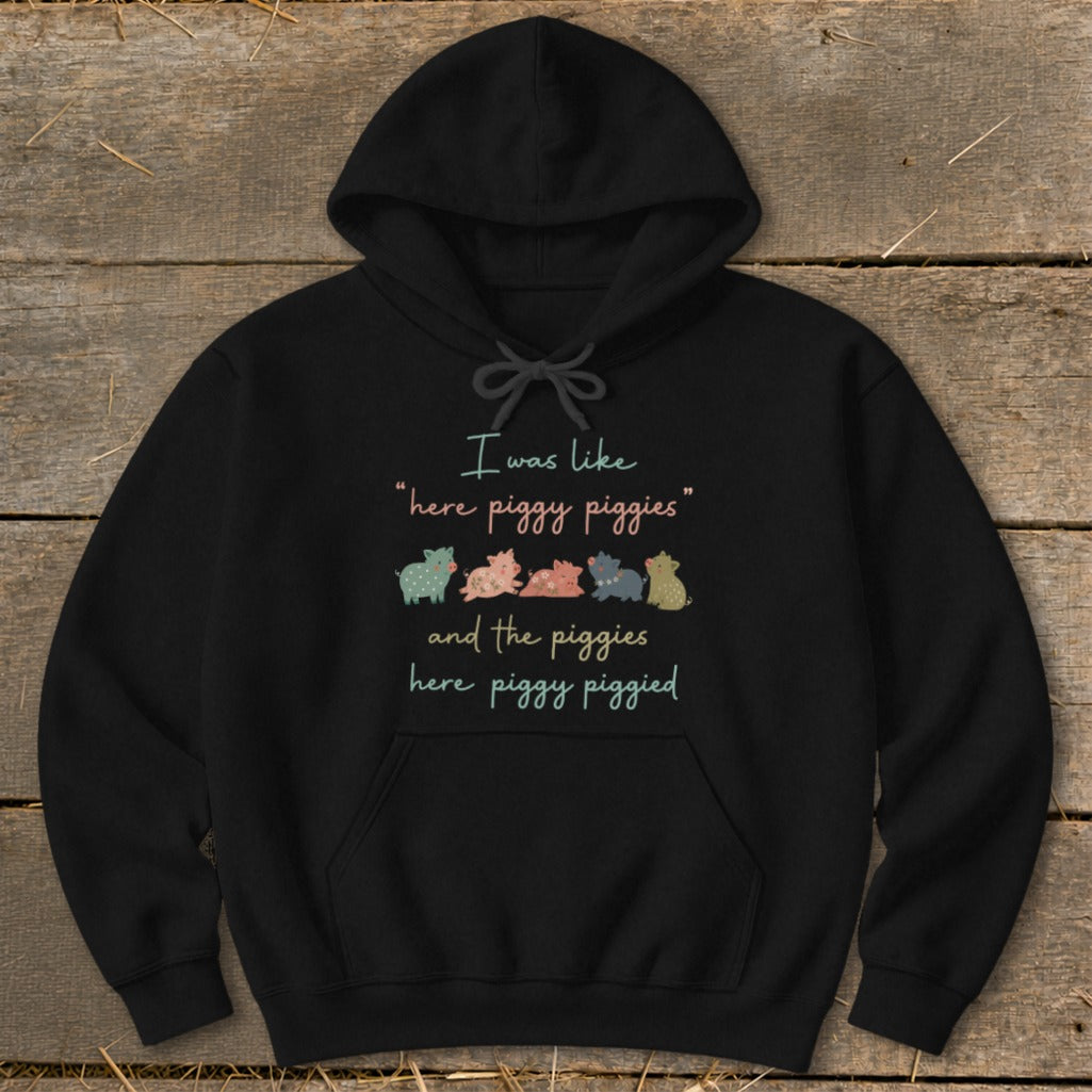 Black hoodie with a text and pig graphic saying "I was like 'here piggy piggies' and the piggies here piggy piggied."