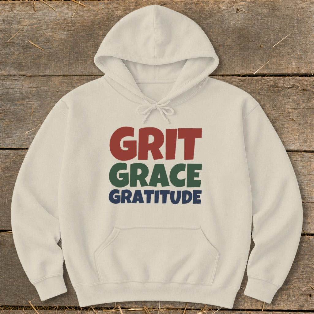 A cream-colored hoodie features the stacked text Grit, Grace, and Gratitude in red, green, and blue.