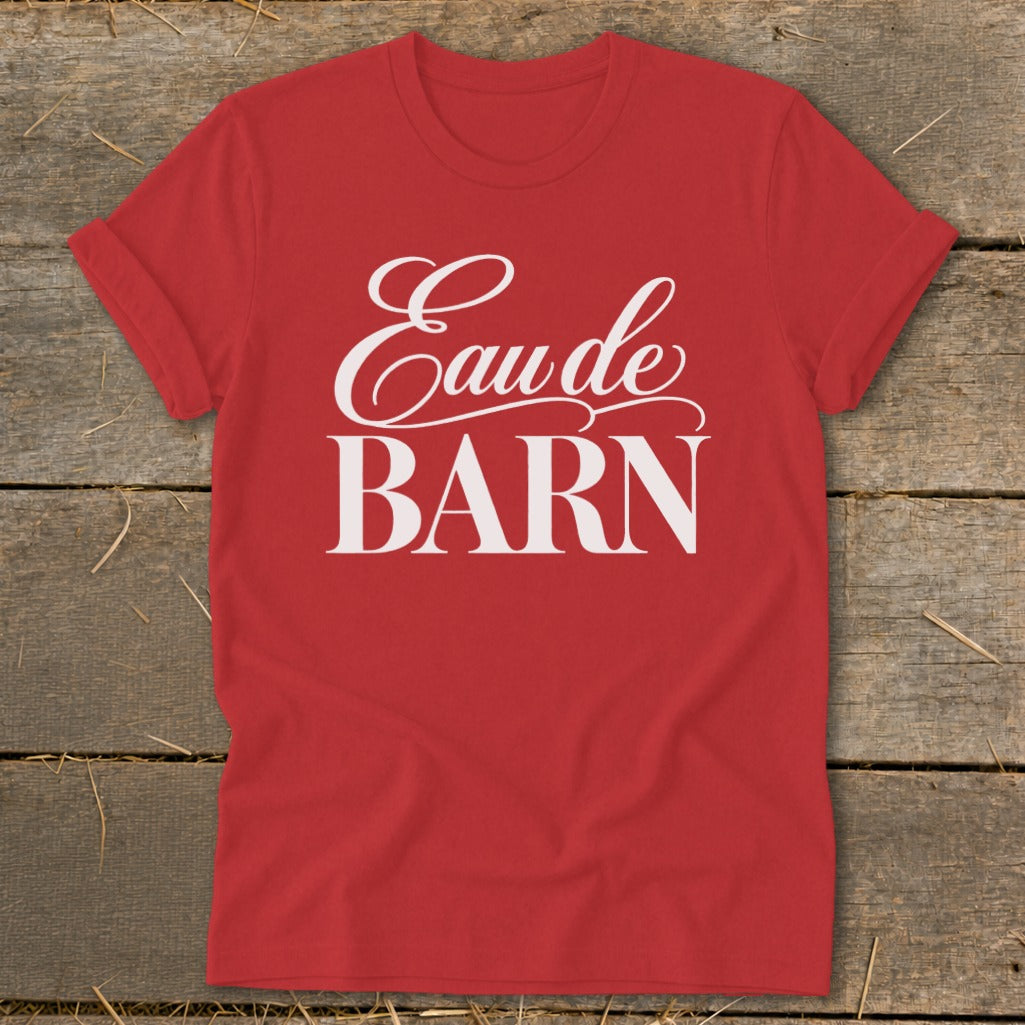 Red t-shirt with white text "Eau de BARN" on rustic wooden background.