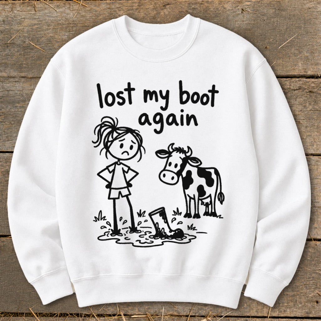 A white sweatshirt with a cartoon graphic of a sad person, a cow, and text reading lost my boot again.
