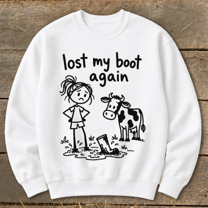 A white sweatshirt with a cartoon graphic of a sad person, a cow, and text reading lost my boot again.