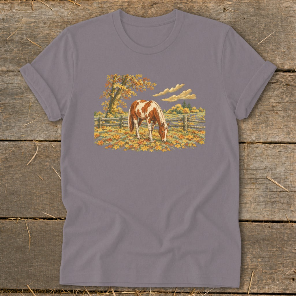 Horse grazing in a field of autumn leaves with a rustic fence and tree.